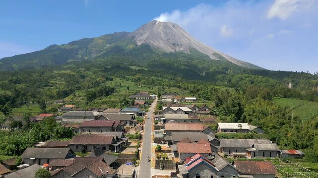 Aerial view of rural village with traditional houses and road leading toward Mount Merapi volcano in Central Java, Indonesia. Scenic landscape showing everyday life near an active volcano.