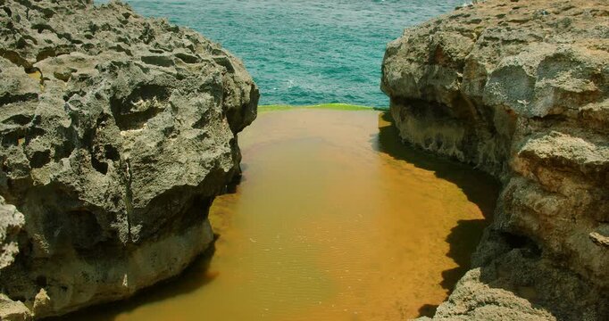 Narrow gap between two large jagged rocks filled with water leading to open ocean at Angel Billabong beach Bali Nusa Penida