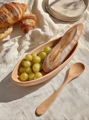 Fresh baked bread and croissants with grapes are arranged on a linen tablecloth.