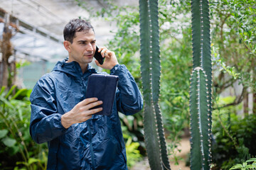 Young scientist in farm environment uses tablet and phone while working with research team focused on agricultural development and plant study in natural setting
