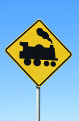 Yellow traffic sign with a black silhouette of a steam train railway crossing against a blue sky background