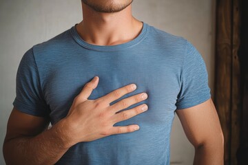 Cropped close-up of a young man in a blue t-shirt with hand over his chest showing sincerity and calm emotion