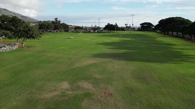 flying over football field with yellow uprights (american touchdown) rural tropical public park in lahaina hawaii (goal scoring green grass) empty nobody team sports game fun athletics high school sky