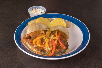 A plate of a Jamaican king fish steak with fired dumplings and vegetables
