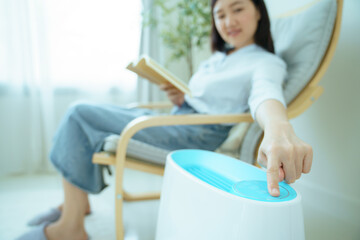 Woman relaxing at home while turning on air purifier at touch control.