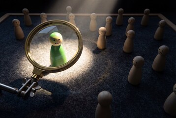 Magnifying glass highlighting single happy green peg doll among many sad wooden figures