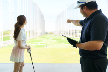 Golf instructor explaining swing technique on digital tablet to woman golfer at driving range.