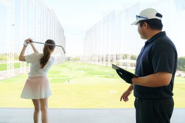 Golf instructor explaining swing technique on digital tablet to woman golfer at driving range.