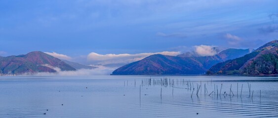 秋の奥琵琶湖の雲海に包まれる紅葉の山々と湖面のパノラマ風景