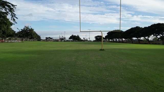 flying over football field with yellow uprights (american touchdown) rural tropical public park in lahaina hawaii (goal scoring green grass) empty nobody team sports game fun athletics high school sky