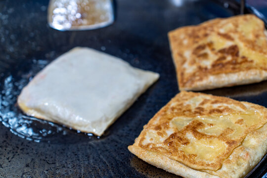 Close-up process of frying Roti Mataba (stuffed flatbread) and crispy roti on a large flat iron pan at a street food stall in Thailand.