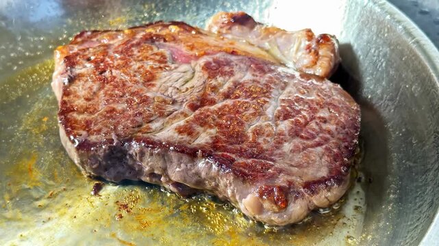 A thick steak sizzles in a hot pan, its browned surface glistening with juices as the heat sears rich texture and color during the cooking process.