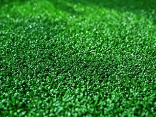 Fototapeta premium Close-up view of dense, vibrant green artificial grass surface with uniform texture and slight shadows creating depth