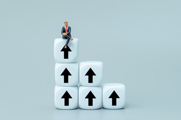 Businessman sits atop a staircase of white cubes marked with upward arrows. Career growth, promotion, personal progress, upskilling concept.