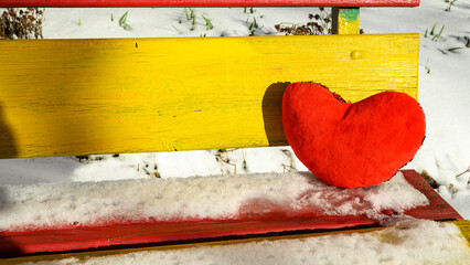 red soft heart on a bright bench under the winter sun