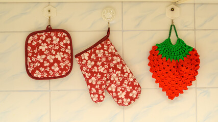 kitchen potholders and a mitten hanging on hooks on the wall