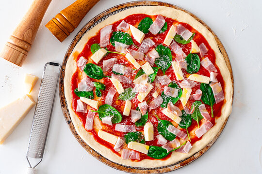 Raw pizza with bacon, tomatoes, cheese and spinach is ready to bake, on a white table. Pizza making process. Top view. High quality photo