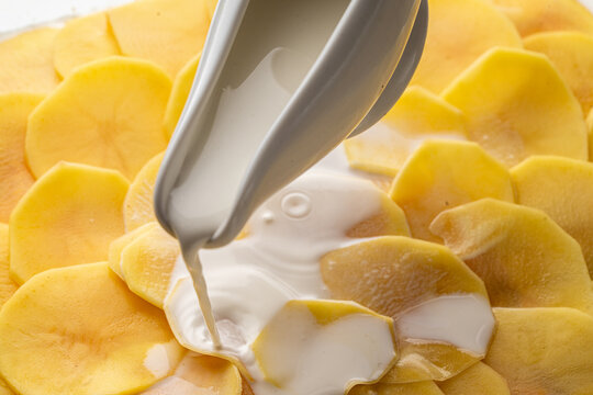 The process of making potato gratin. Delicate cream is poured over raw, thin potato slices. High quality photo