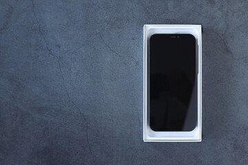 Concept for giving, technology, unboxing and shopping, and advertising. Top view, flat lay new smartphone in white box over dark concrete background with copy space