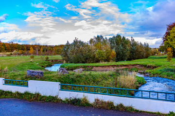 Autumn landscape of Absbroekbos nature conservation area seen from vehicular bridge over Geleenbeek River, trees with yellowish-green foliage in background, Munstergeleen, Limburg, Netherlands