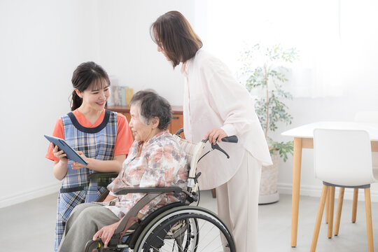 在宅介護や訪問介護のデイサービスのイメージで訪問する看護師と後期高齢者の女性と家族　訪問介護の計画などをタブレットで案内する