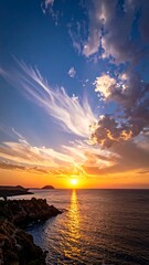 Fiery sunset over the sea, with whispy clouds and rocky shoreline, glowing with orange light
