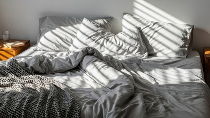Sunlit unmade bed with wrinkled sheets and blanket in cozy bedroom interior with natural light