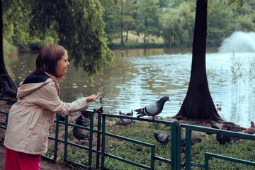 Happy Little Girl Plays with Pigeons in the Park. Kid having a lot of fun observing the urban birds by the lake
