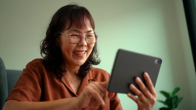 Happy senior woman using tablet at home with digital technology engagement lifestyle, older female texting and online connected with family, retired communication in daily life with wellbeing at home.