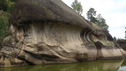 Unique rock formation next to a calm river surrounded by lush greenery