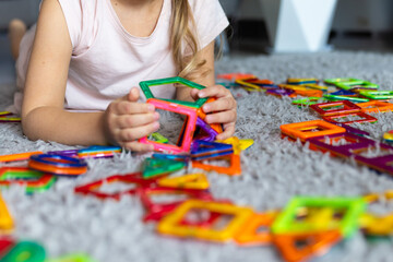 Naklejka premium Young girl playing with colorful magnetic building tiles on a carpet at home