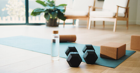 House, mat and dumbbells with glass bottle for fitness training, exercise equipment and workout gear. Weights, yoga brick and water for hydration in home gym, pilates supplies and beverage on floor