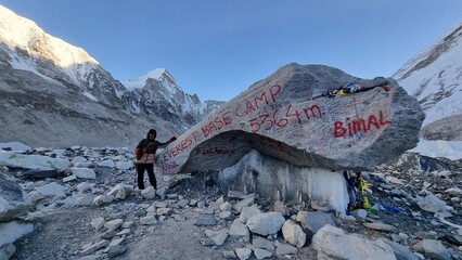A lone hiker stands beside a massive boulder marked with Everest Base Camp and altitude, showcasing the rugged beauty of the Himalayas © MdAbu