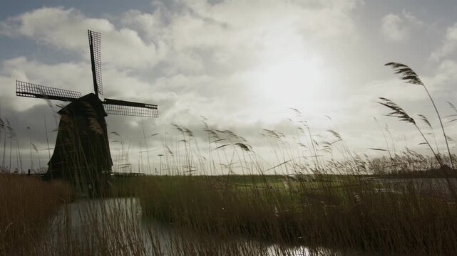 Wide view of a historic windmill standing in a rural landscape with reeds, water and a calm sky, conveying traditional heritage, countryside atmosphere and timeless scenery.