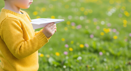 Young boy holding paper plane in spring field with copy space for text