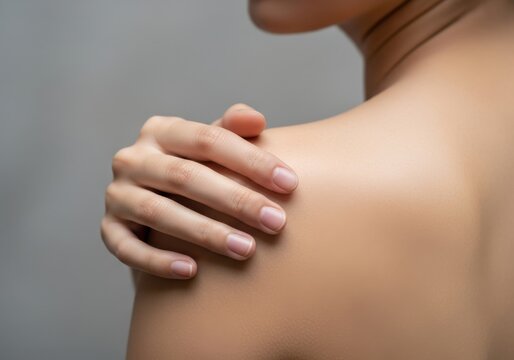 Closeup of a persons hand touching their shoulder with a visible red spot on the skin