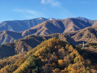 The mountains are covered in a variety of trees, including some that are orange and yellow. The sky is clear and blue, with no clouds in sight. Scene is calm and tranquil