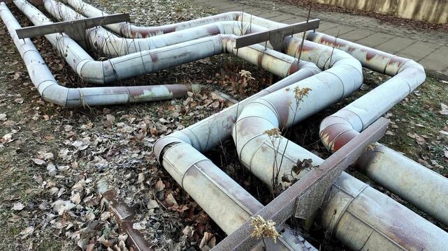 Frost covered damaged and vandalized district heating pipes running above ground in a neglected urban area during winter
