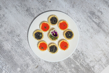 Plate of assorted caviar tarts with floral garnish on textured background
