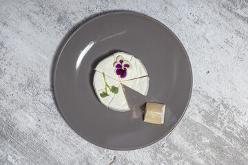 Top view of round goat cheese elegantly garnished with edible flowers on a gray plate on a textured...