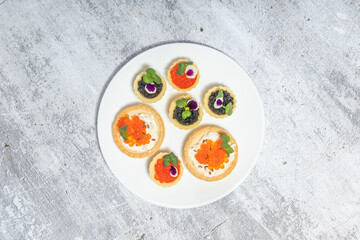 Elegant plate of gourmet canap&eacute;s featuring caviar and cream cheese on crackers, garnished with herbs and edible flowers.