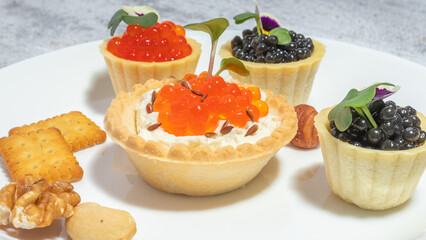 Assorted caviar tartlets on a plate with nuts and crackers, showcasing gourmet appetizers in an elegant presentation.
