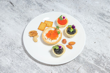 Plate with gourmet appetizers featuring red and black caviar, nuts, and crackers on a textured background.