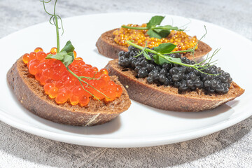 Assorted caviar on slices of dark bread garnished with pea shoots on a white plate