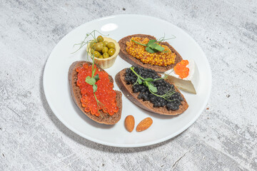 Assorted gourmet appetizers on a white plate featuring caviar, mustard, olives, and cheese on rustic bread.
