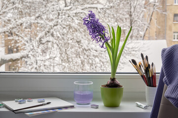 Cozy winter windowsill with hyacinth, art supplies and urban view.
