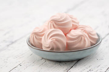 Close up of several pink homemade zefir marshmallow confection in a small blue bowl, served on a distressed white rustic wooden table. Meringue cookies  on a plate. Copy space for text.