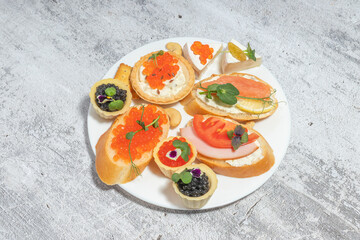 An elegant assortment of canap&eacute;s on a white plate featuring various toppings like caviar, salmon, and cheese over a textured background.