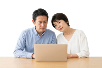 Asian couple sitting at table looking at laptop computer together isolated on transparent background