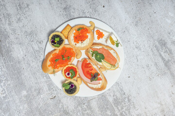 Plate with various appetizers including caviar, salmon, and vegetables on rustic background